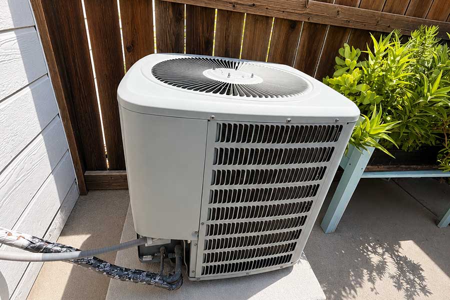 Outdoor AC condenser beside a fence and landscaping for AC installation