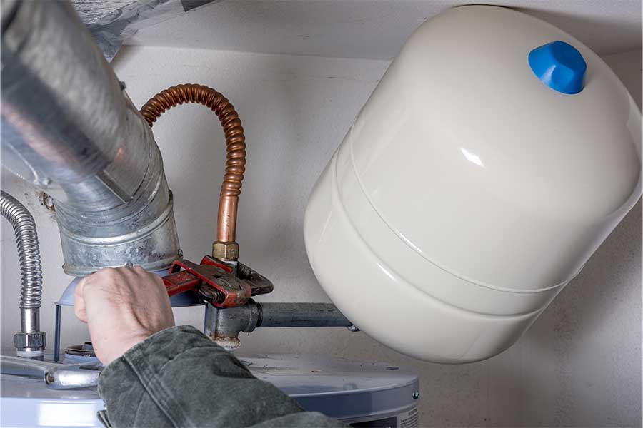 Plumber repairing a commercial water heater connection with a pipe wrench beside an expansion tank