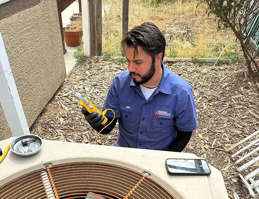 Technician diagnosing an outdoor condenser with a test meter during emergency HVAC repair in Vacaville, CA
