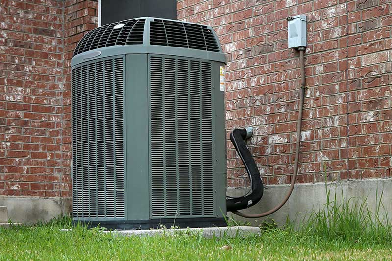 Gray outdoor heat pump installed beside a brick wall in Vacaville