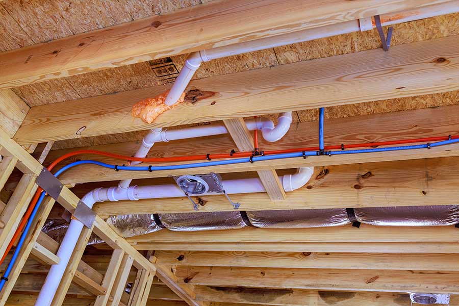 Red and blue PEX water lines routed through exposed wood framing during home repiping in Vacaville