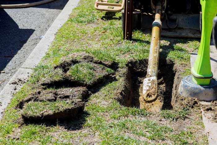 Trenchless sewer replacement equipment positioned over a small access pit in a lawn