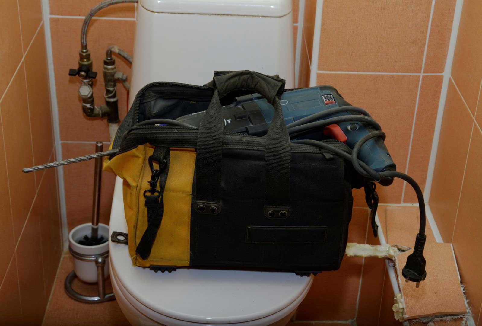 Plumber’s bag and repair tools on top of a toilet during leaking toilet service